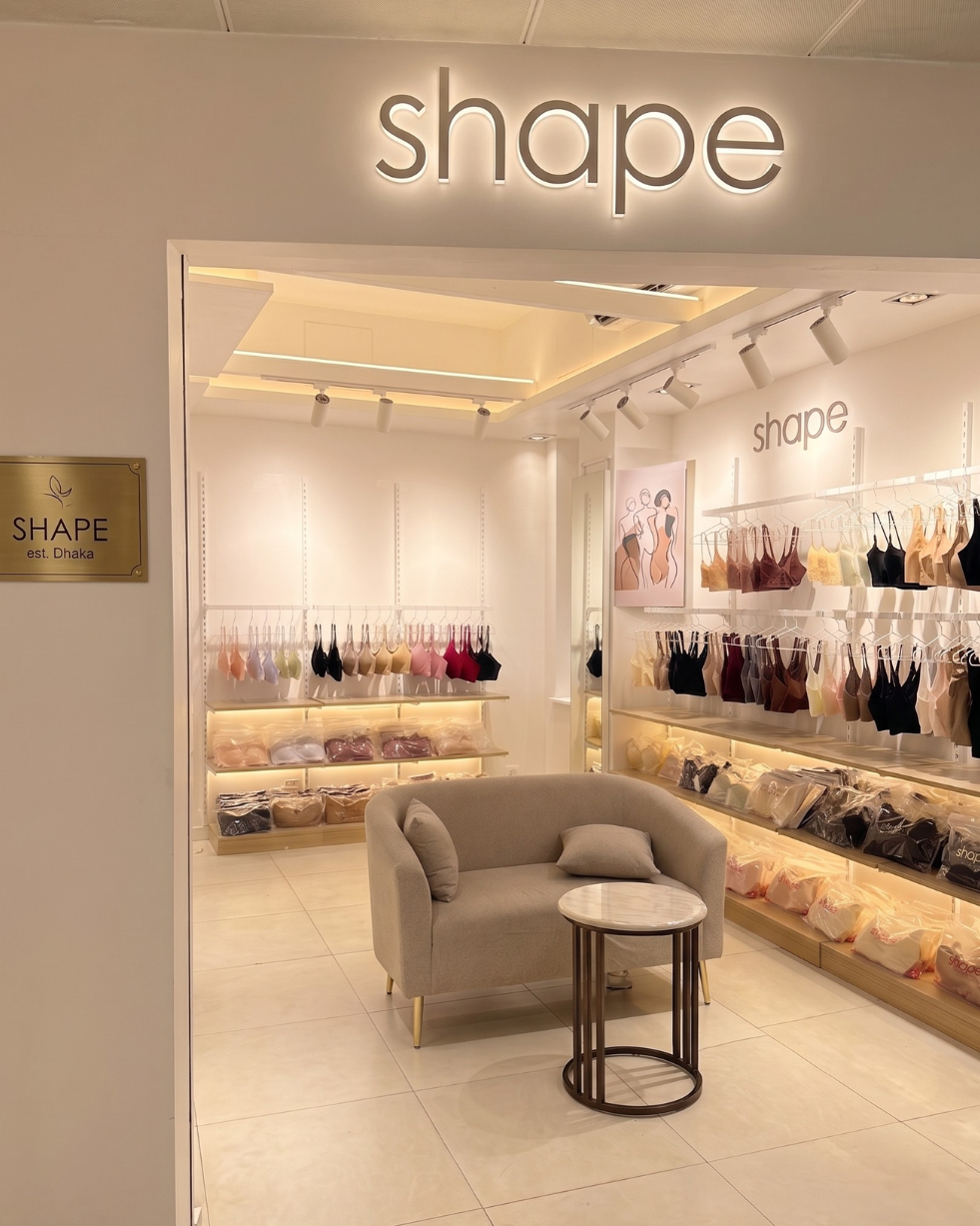 Store interior on Siraj Capital, Bailey Road, Dhaka, with SHAPE Lingerie bras displayed on wall racks and a private seating area.